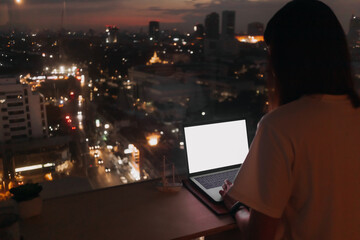 Asian woman work with laptop by the windows apartment with evening city view.