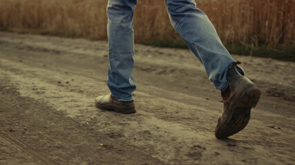 Man farmer legs in shoes passing farmland rural road. Rubber boots close up.
