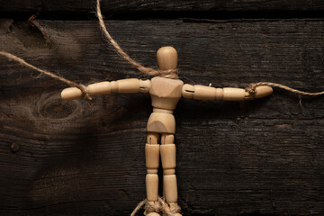 wooden man on ropes on a wooden background, tied to a man's hand, manipulation of people and...