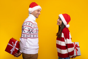 Close up photo of smiling excited young couple in love in Christmas clothes while they standing and hiding presents from each other behind back