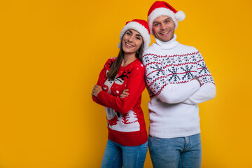 Fototapeta premium Close up photo of excited young couple in love in winter sweaters and Christmas Santa hats while they having fun and posing isolated on yellow background