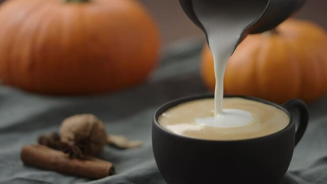 Slow motion making spiced pumpkin latte in black cup, pour steamed milk
