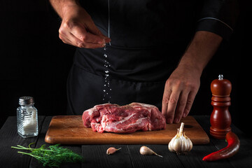 Professional chef sprinkles the meat with salt. Preparing meat before baking. Working environment in the kitchen of restaurant