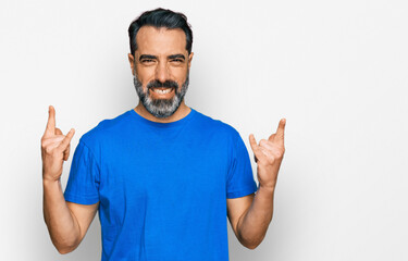 Fototapeta premium Middle aged man with beard wearing casual blue t shirt shouting with crazy expression doing rock symbol with hands up. music star. heavy concept.