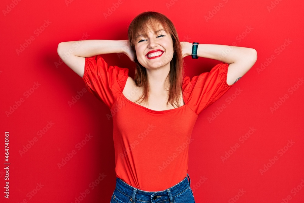 Sticker Redhead young woman wearing casual red t shirt relaxing and stretching, arms and hands behind head and neck smiling happy