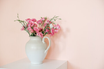 Bouquet with eustoma, summer flowers in a white vase, on a pink-beige background.