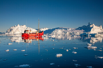 Red boat amongst icebergs in Disko Bay, Greenland