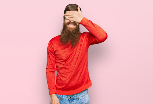 Redhead man with long beard wearing casual clothes smiling and laughing with hand on face covering eyes for surprise. blind concept.