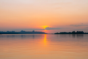 Calm water surface with pink sunset sky and sun through the clouds over. Meditation water and yellow sky background. Horizon over the water.