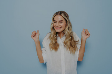 Blonde girl with closed eyes cheering with both hands in air