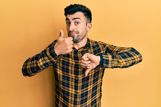 Young hispanic man wearing casual clothes doing thumbs up and down, disagreement and agreement expression. crazy conflict