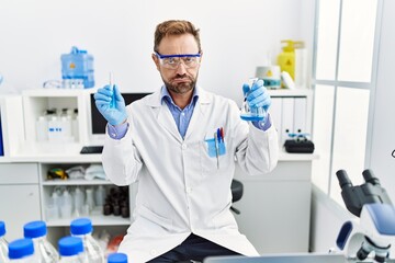 Middle age man working at scientist laboratory holding chemical products depressed and worry for distress, crying angry and afraid. sad expression.