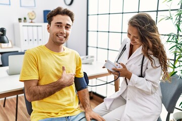 Young doctor woman checking blood pressure on patient smiling happy pointing with hand and finger