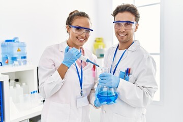 Man and woman wearing scientist uniform using pipette and test tube working at laboratory