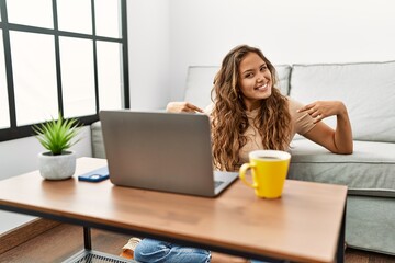 Beautiful hispanic woman using computer laptop at home looking confident with smile on face,...