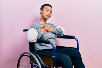 Obraz na płótnie Canvas Beautiful hispanic woman with short hair sitting on wheelchair smiling with hands on chest with closed eyes and grateful gesture on face. health concept.