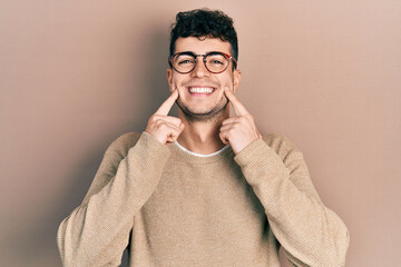 Young hispanic man wearing casual clothes and glasses smiling with open mouth, fingers pointing and forcing cheerful smile
