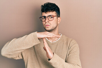 Young hispanic man wearing casual clothes and glasses doing time out gesture with hands, frustrated...