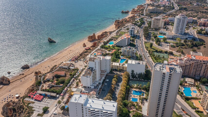 Obraz na płótnie Canvas Aerial view of the city of Portimao over residential buildings, high-rise buildings, on the beach Praia de Rocha with tourists.