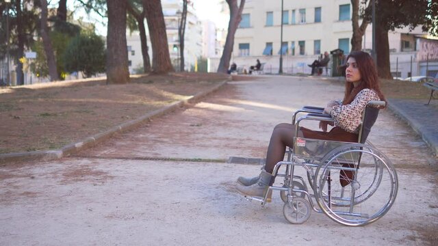 solitude, disability- young woman using wheelchair alone at park looks up
