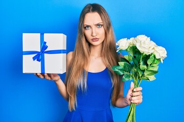 Young blonde girl holding anniversary present and bouquet of flowers skeptic and nervous, frowning...