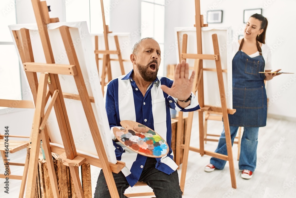 Sticker senior artist man at art studio doing stop gesture with hands palms, angry and frustration expressio