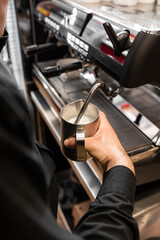 Barista heats milk with high-pressure steam for making lattes. Flowing fresh ground coffee. Drinking roasted black coffee in the morning.