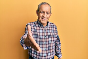 Handsome senior man with grey hair wearing casual shirt smiling friendly offering handshake as greeting and welcoming. successful business.