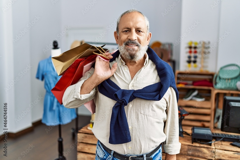 Sticker handsome senior man holding shopping bags at boutique shop looking positive and happy standing and s