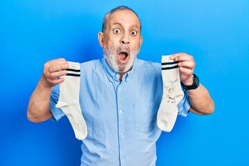 Handsome senior man with beard holding clean andy dirty socks afraid and shocked with surprise and...