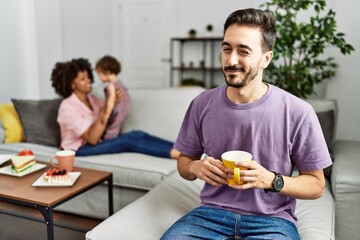 Hispanic father of interracial family drinking a cup coffee winking looking at the camera with sexy expression, cheerful and happy face.