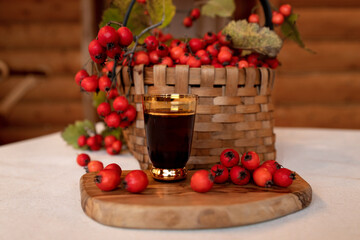A wicker basket full of red ripe hawthorn berries, next to a glass with a tincture of hawthorn. Medicinal drinks, folk medicine.