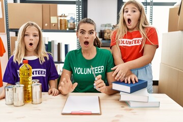 Young woman with two daughters wearing volunteer t shirt at donations stand scared and amazed with...