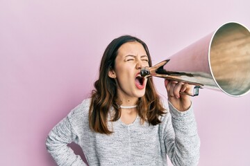 Young brunette woman shouting and screaming through vintage megaphone over pink isolated background - obrazy, fototapety, plakaty
