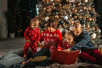 Fototapeta na wymiar Christmas night, beautiful family reading a book at the foot of the tree