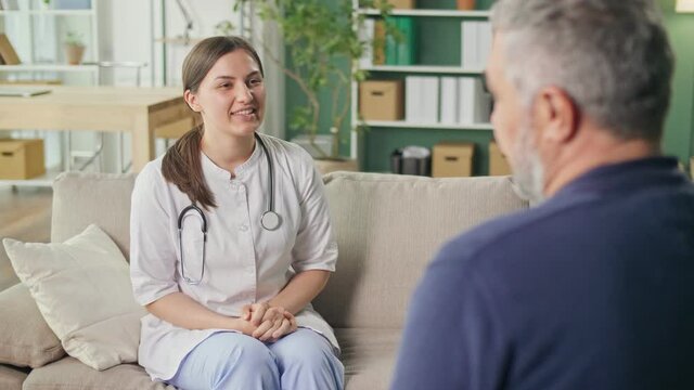 A Friendly Medical Professional Takes Care of a Middle-aged Man at Home. Medical Services, Rehabilitation, Consultation of a Medical Worker at Home. Pension Insurance and Health Care Concept.