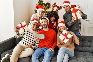 Group of young people drinking wine and holding gifts make selfie by the smartphone at home.