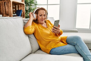 Obraz premium Middle age caucasian woman listening to music sitting on the sofa at home.