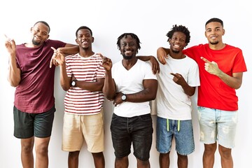 Young african group of friends standing together over isolated background with a big smile on face, pointing with hand finger to the side looking at the camera.