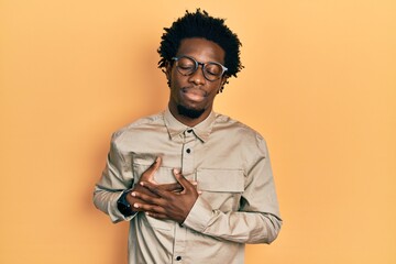 Young african american man wearing casual clothes and glasses smiling with hands on chest with closed eyes and grateful gesture on face. health concept.