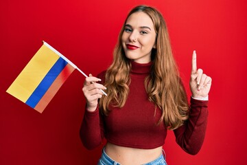 Young blonde woman holding colombia flag smiling with an idea or question pointing finger with happy face, number one