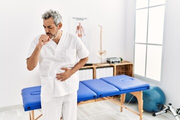 Obraz premium Middle age hispanic therapist man working at pain recovery clinic feeling unwell and coughing as symptom for cold or bronchitis. health care concept.