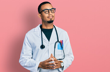 Young african american man wearing doctor uniform and stethoscope hands together and fingers crossed smiling relaxed and cheerful. success and optimistic