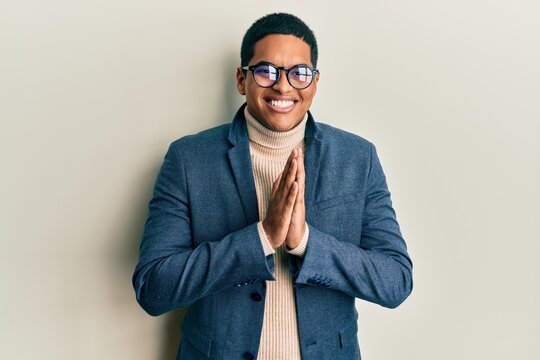 Young handsome hispanic man wearing elegant clothes and glasses praying with hands together asking for forgiveness smiling confident.