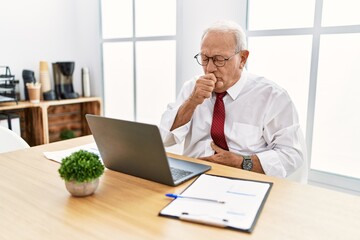 Senior man working at the office using computer laptop feeling unwell and coughing as symptom for cold or bronchitis. health care concept.