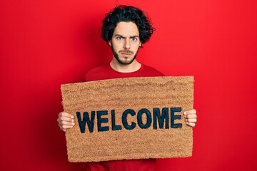 Handsome hispanic man holding welcome doormat skeptic and nervous, frowning upset because of problem. negative person. © Krakenimages.com