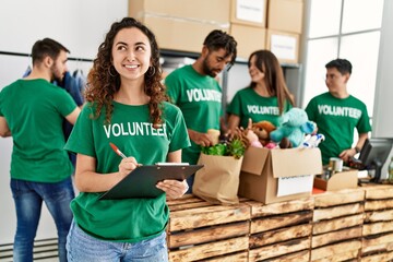 Group of young volunteers working at charity center. Woman smiling happy writing on clipboard.