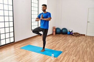 Handsome hispanic man doing exercise and stretching on yoga mat, practicing flexibility and training at the gym