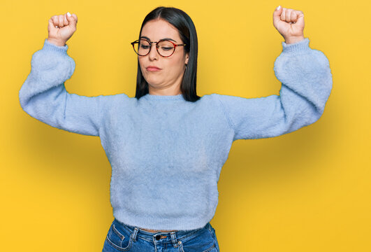 Young hispanic woman wearing casual clothes and glasses showing arms muscles smiling proud. fitness concept.
