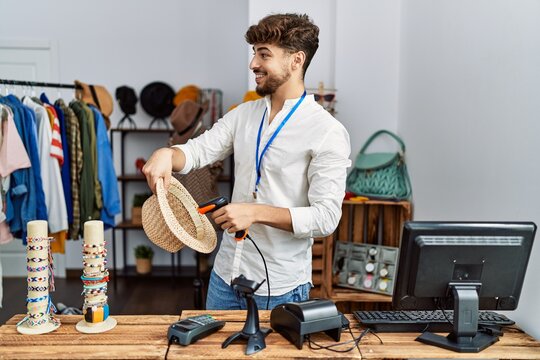 Young arab man smiling confident scanning hat using barcode reader at clothing store